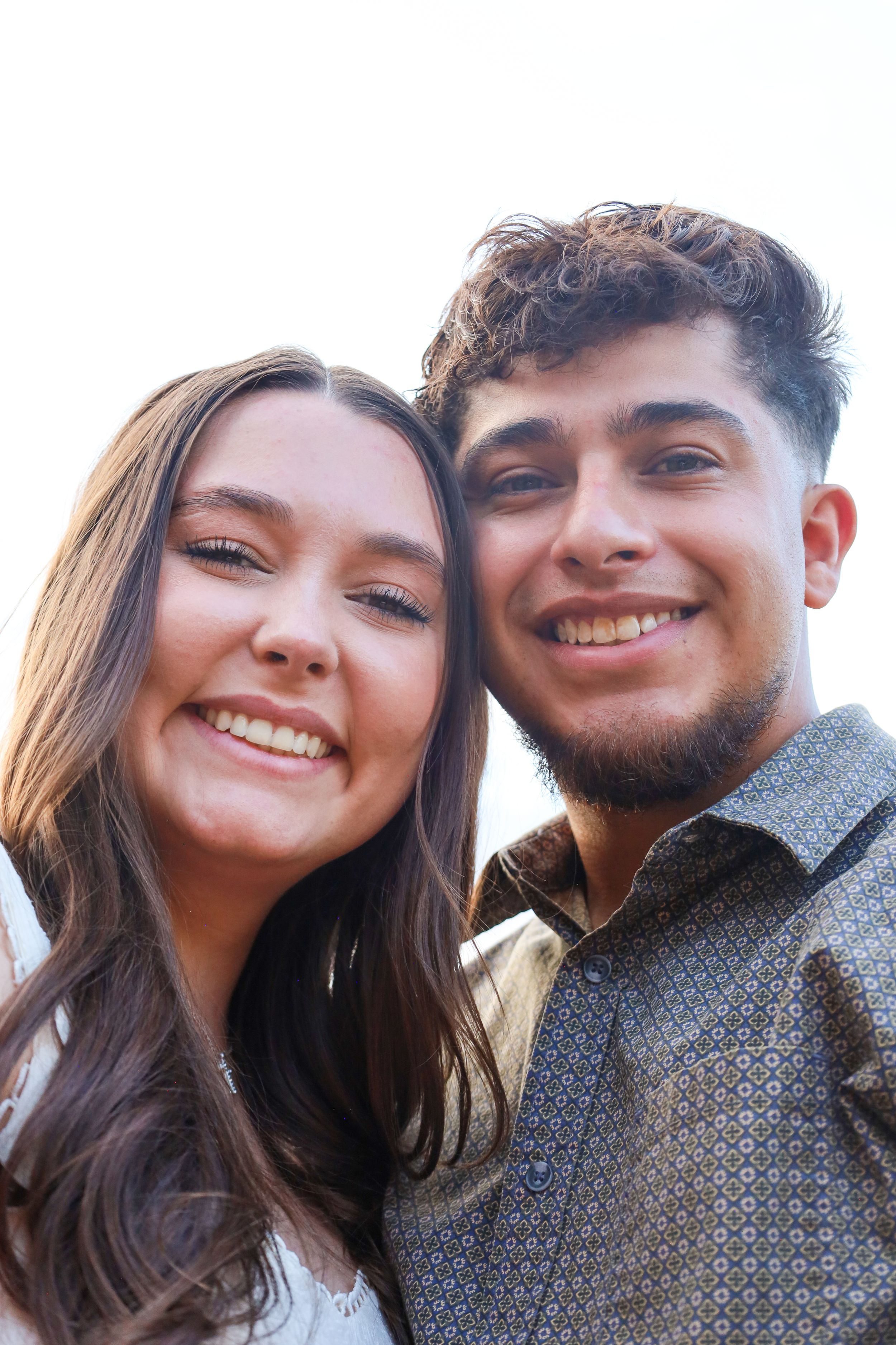 Young smiling couple posing closely together for a selfie photo outdoors.