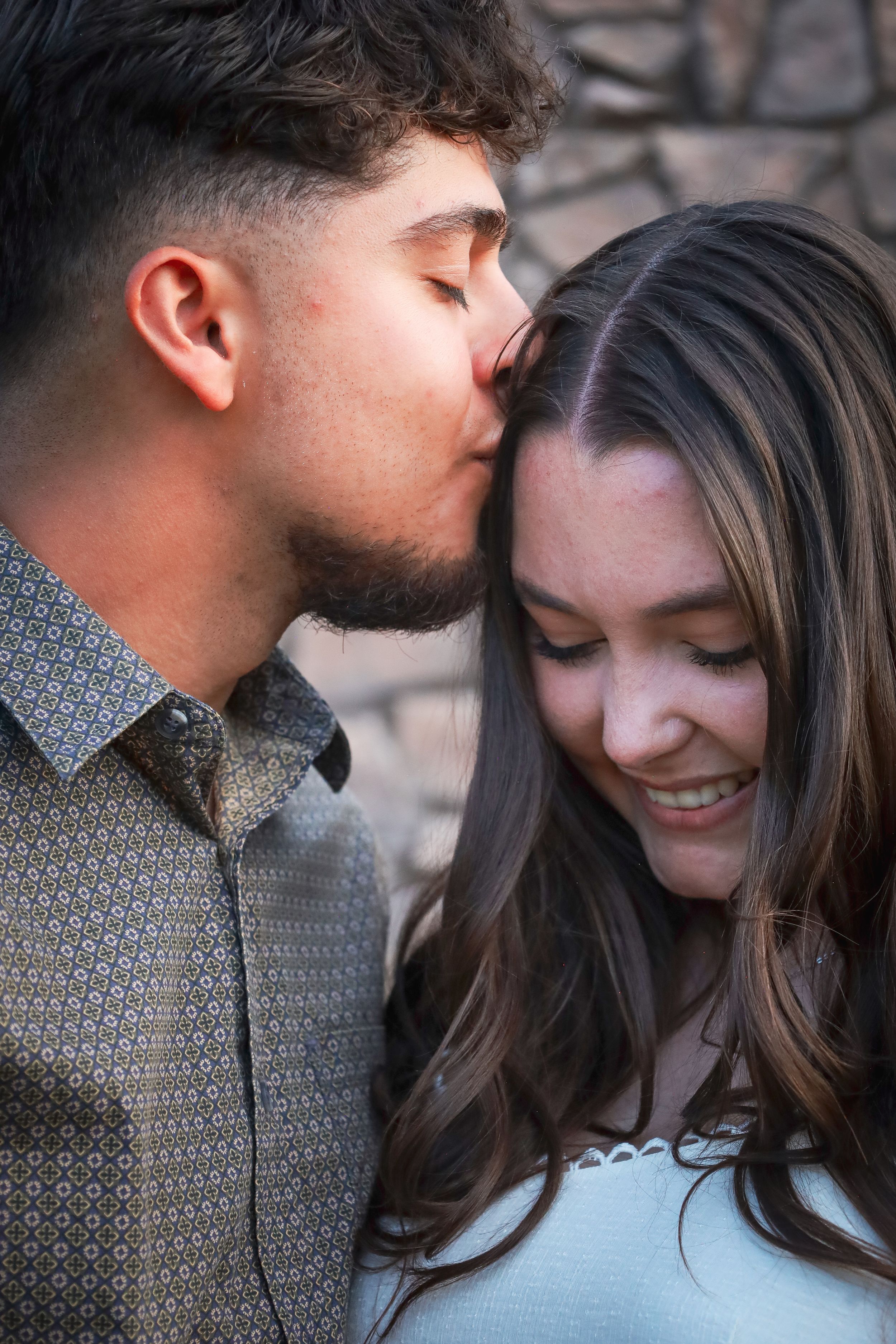Young man kissing woman on the forehead while she smiles during romantic photo session.