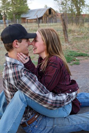 Young couple sitting close together about to kiss near a rustic barn on a farm.
