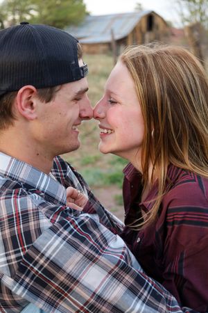 Smiling young couple nose to nose sharing a romantic moment near a rustic barn.