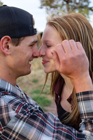 Young couple touching noses and smiling intimately outdoors near a rustic barn.