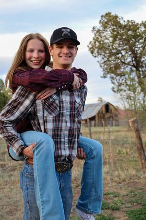 Young man giving his girlfriend a piggyback ride near a rustic barn on a farm.
