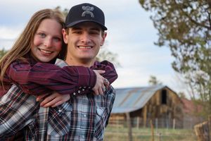 Smiling young couple posing together with a rustic barn in the background on a farm.