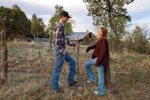 Young couple standing by a rustic fence in a rural farm setting surrounded by trees in autumn.