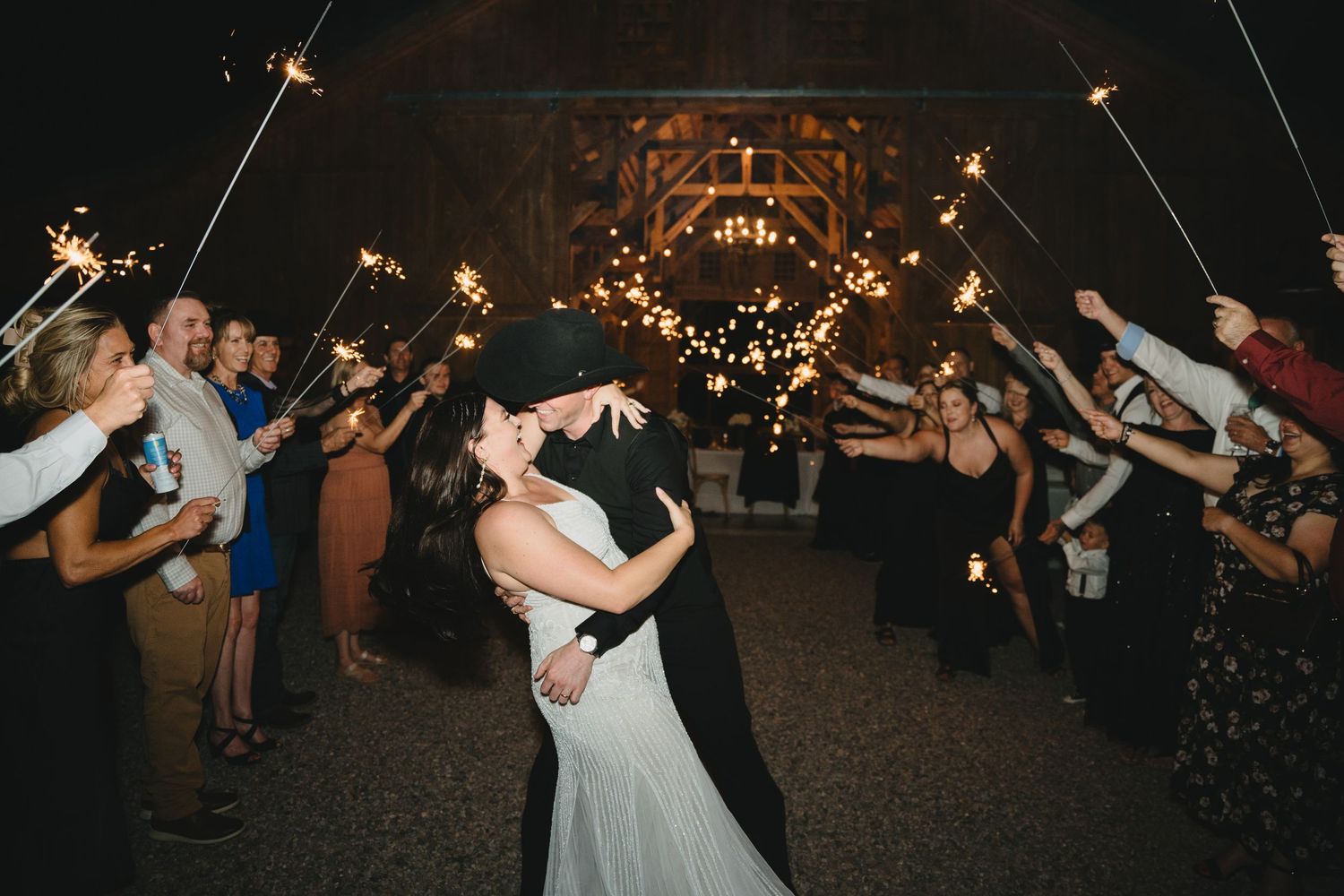 Bride and groom kiss during sparkler send-off exit at nighttime barn wedding celebration. Chama Log River Ranch cinematic photography