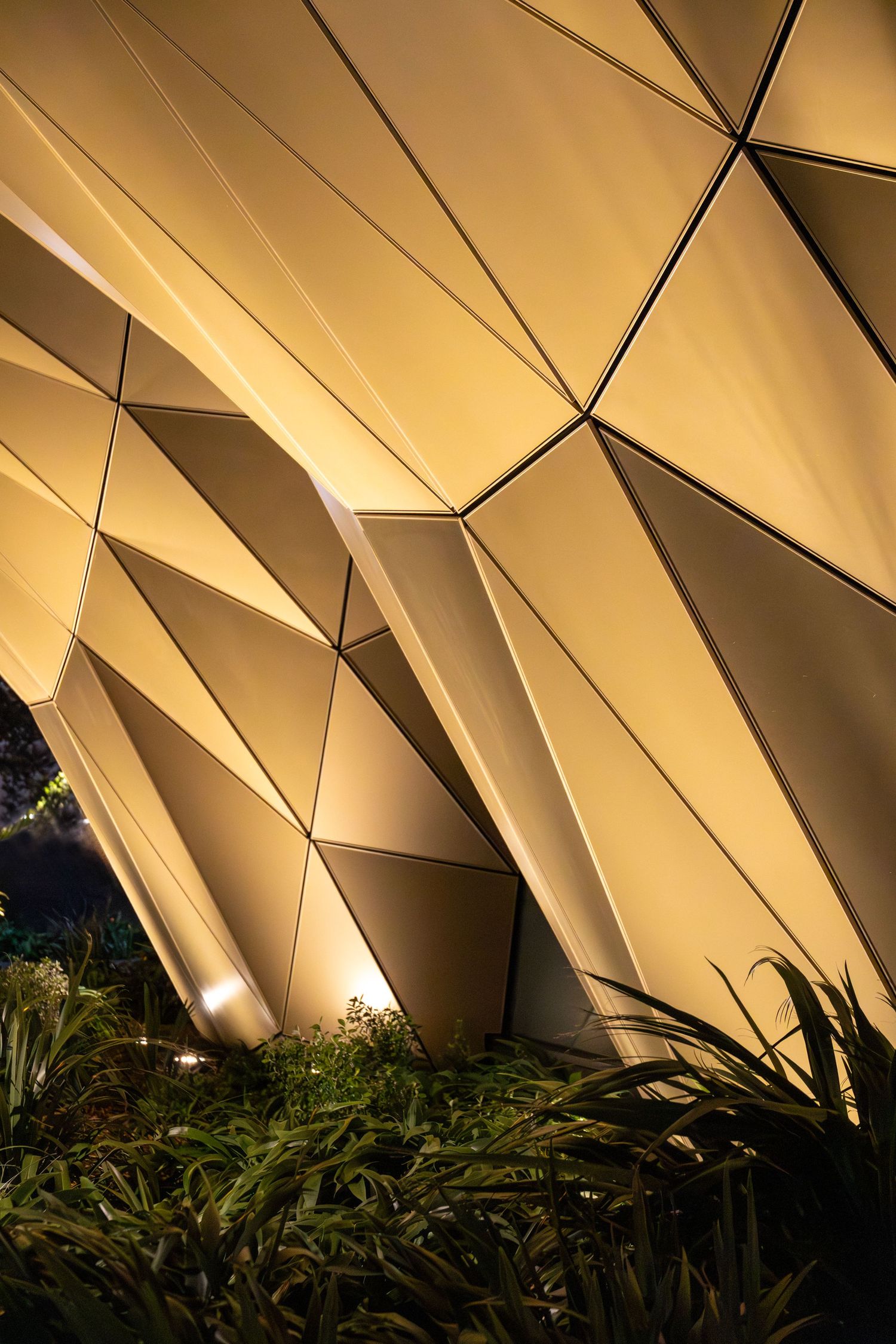 Illuminated golden folds of angular architectural cladding glowing after dark.