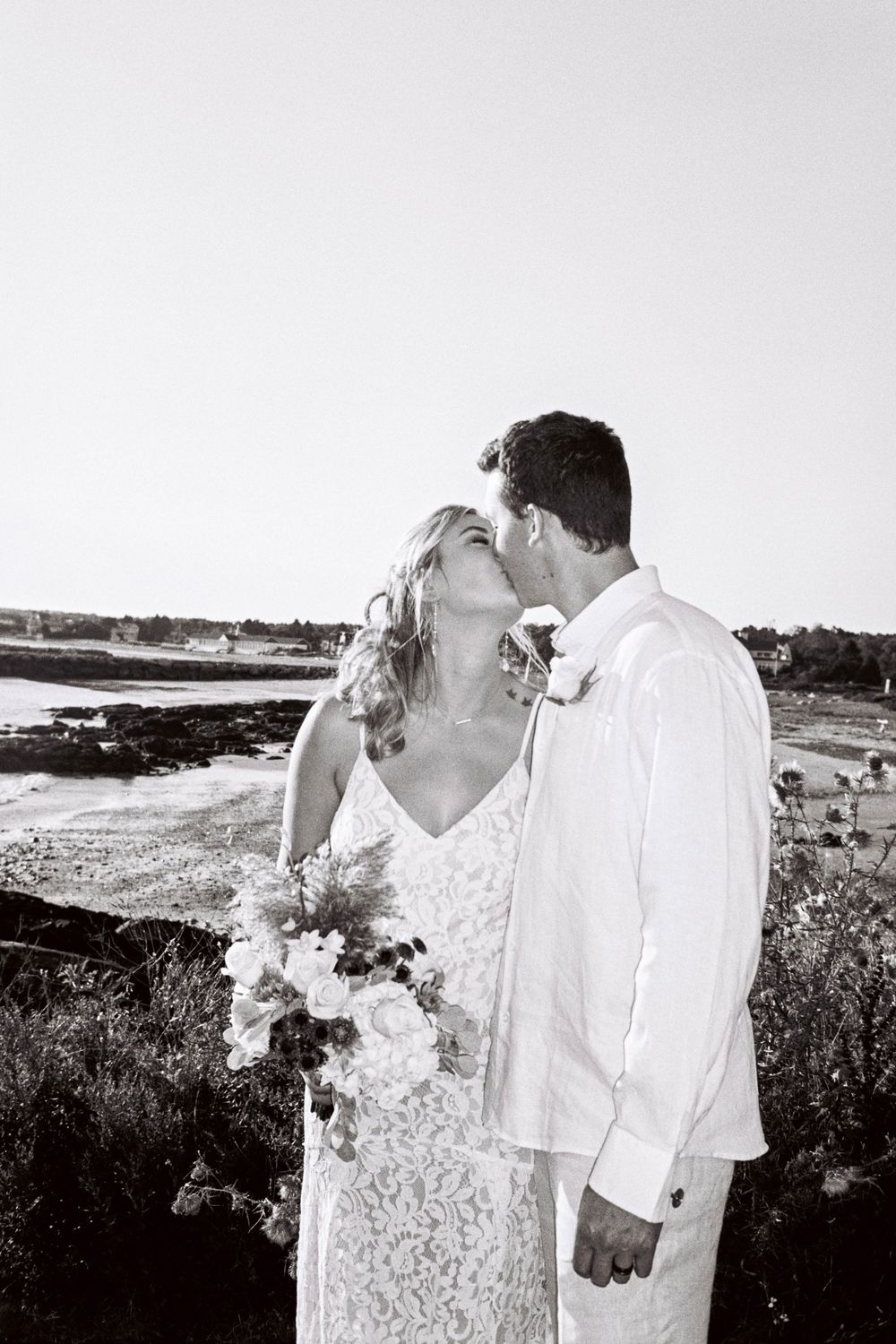 A couple kisses while she holds her bouquet next to the ocean on a late summers day on 35mm film in Kennebunkport, Maine.