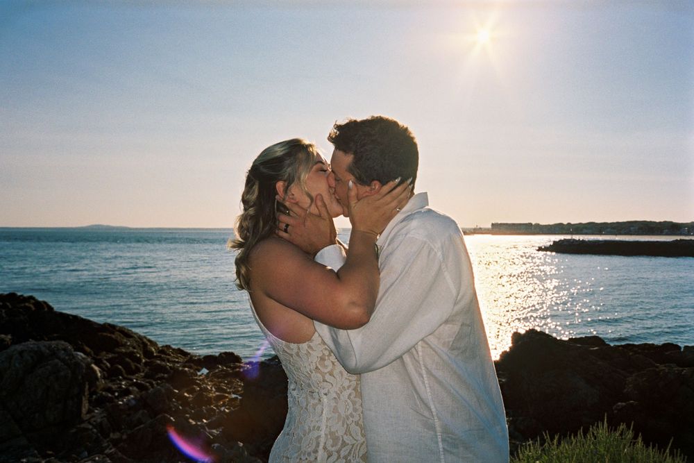 A couple holds eachother's faces as they kiss after their marriage ceremony under the sun by the sea on 35mm film in Kennebunkport, Maine.