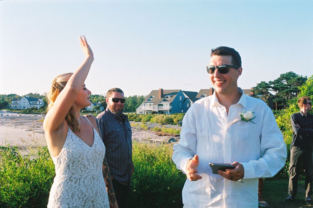 She waves, he smiles as they celebrate their wedding ceremony and send love to their friends and family by the beach in Kennebunkport, Maine