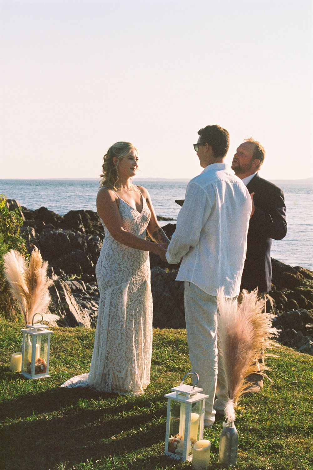 A couple holds hands while their officiant speaks about their love during their intimate beachside wedding ceremony in southern Maine.