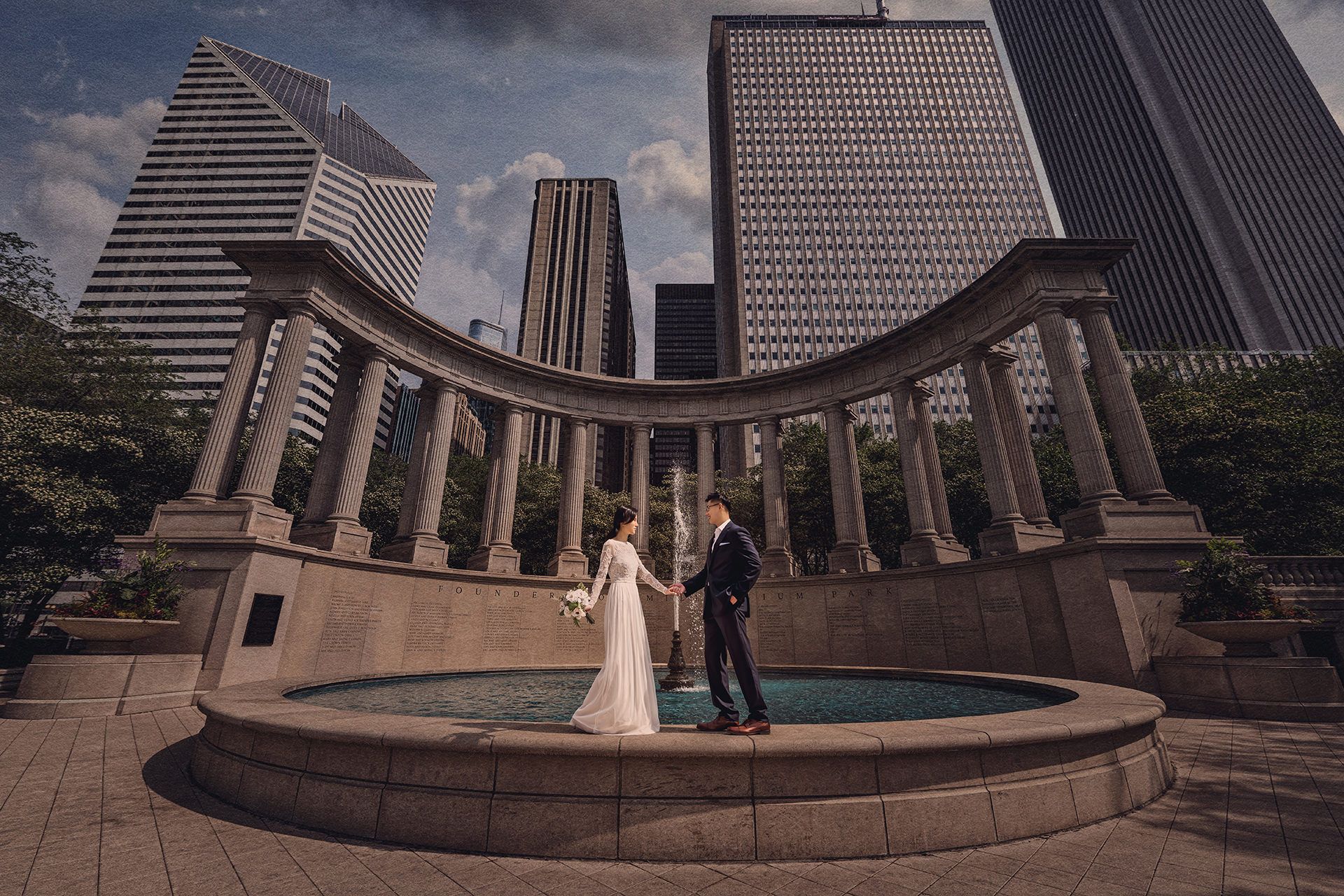 A couple in wedding attire shares a moment at the Millennium Monument in Chicago with skyscrapers towering in the background.