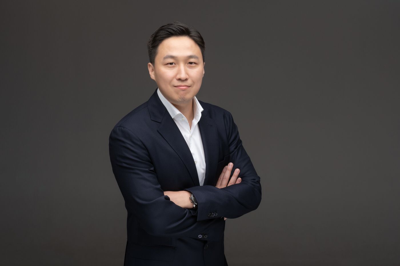 Professional headshot featuring someone in business attire against a dark gray studio backdrop.