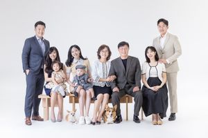 A multi-generational family group with a pet dog sits together for a formal portrait against a white backdrop.