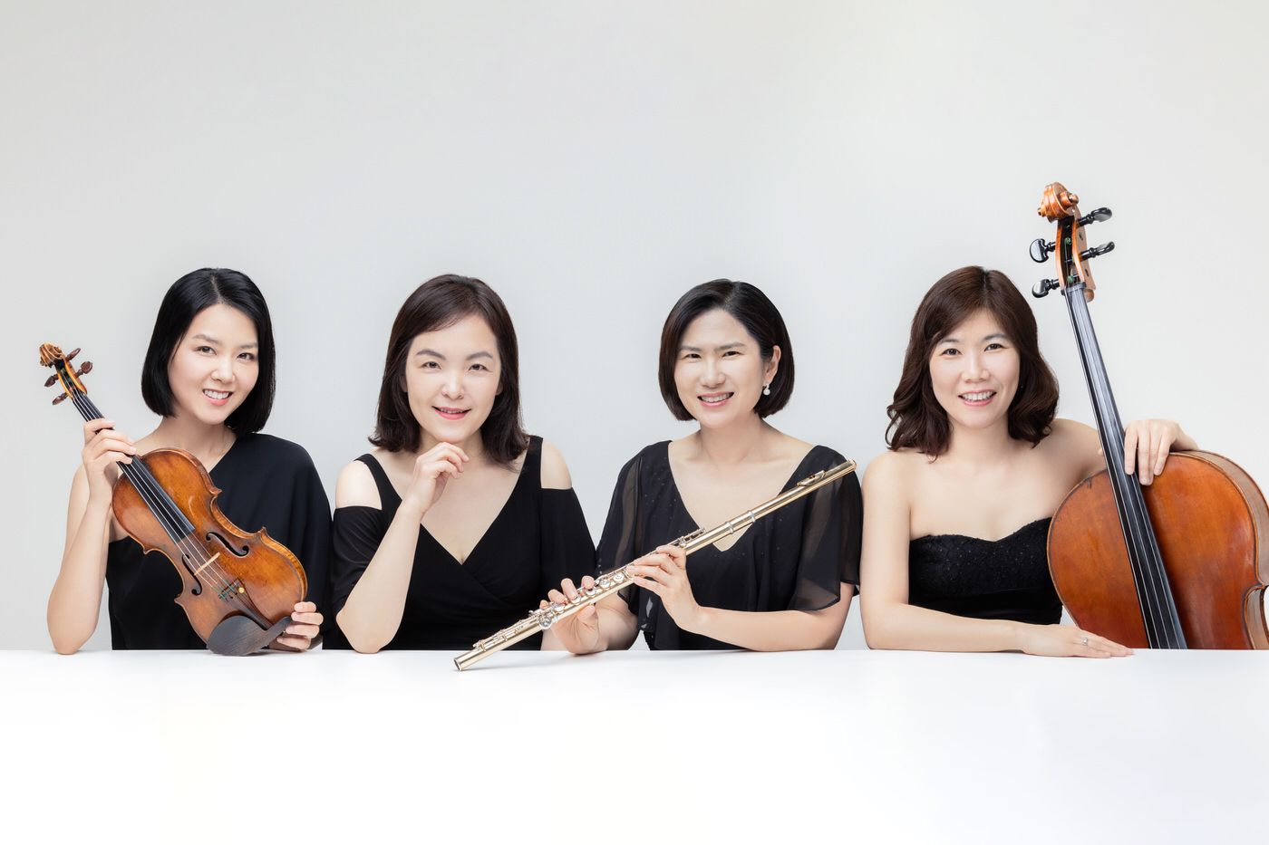 A classical music quartet ensemble in black formal attire poses with their string instruments against a white backdrop.