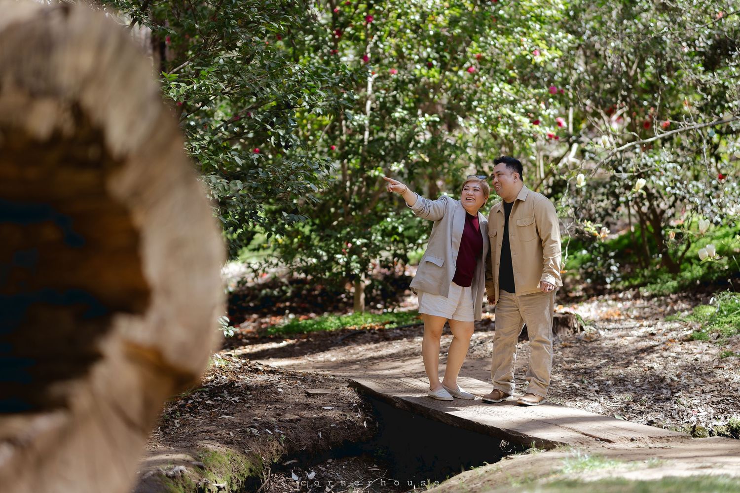 Two people in light clothing walk along a shaded woodland path on a sunny afternoon.