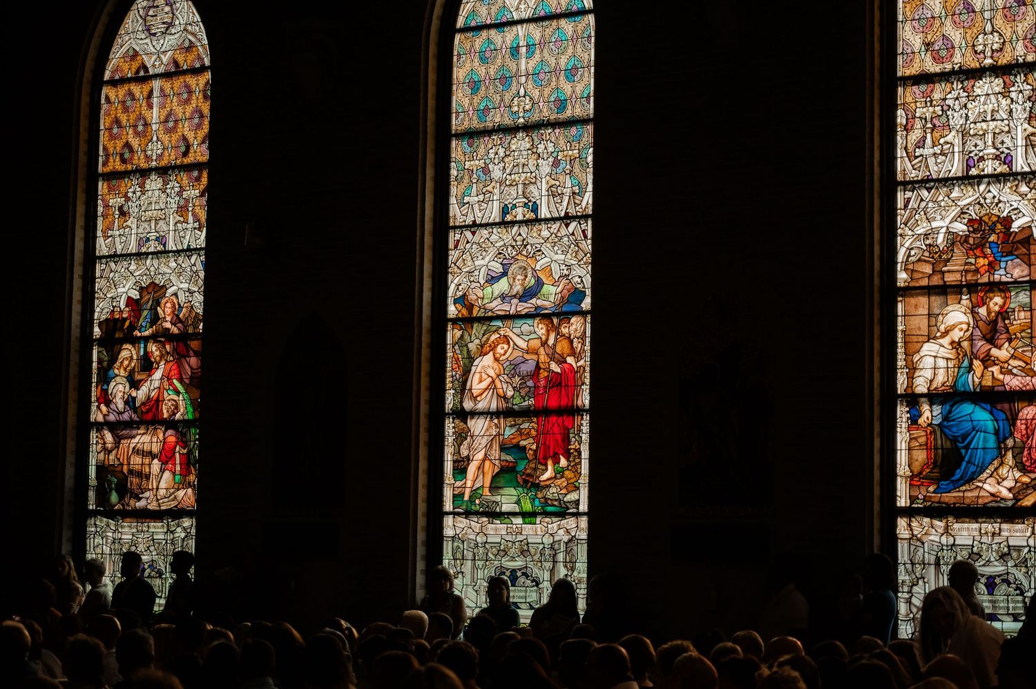 Stained glass church windows depicting biblical scenes with silhouettes of people below.