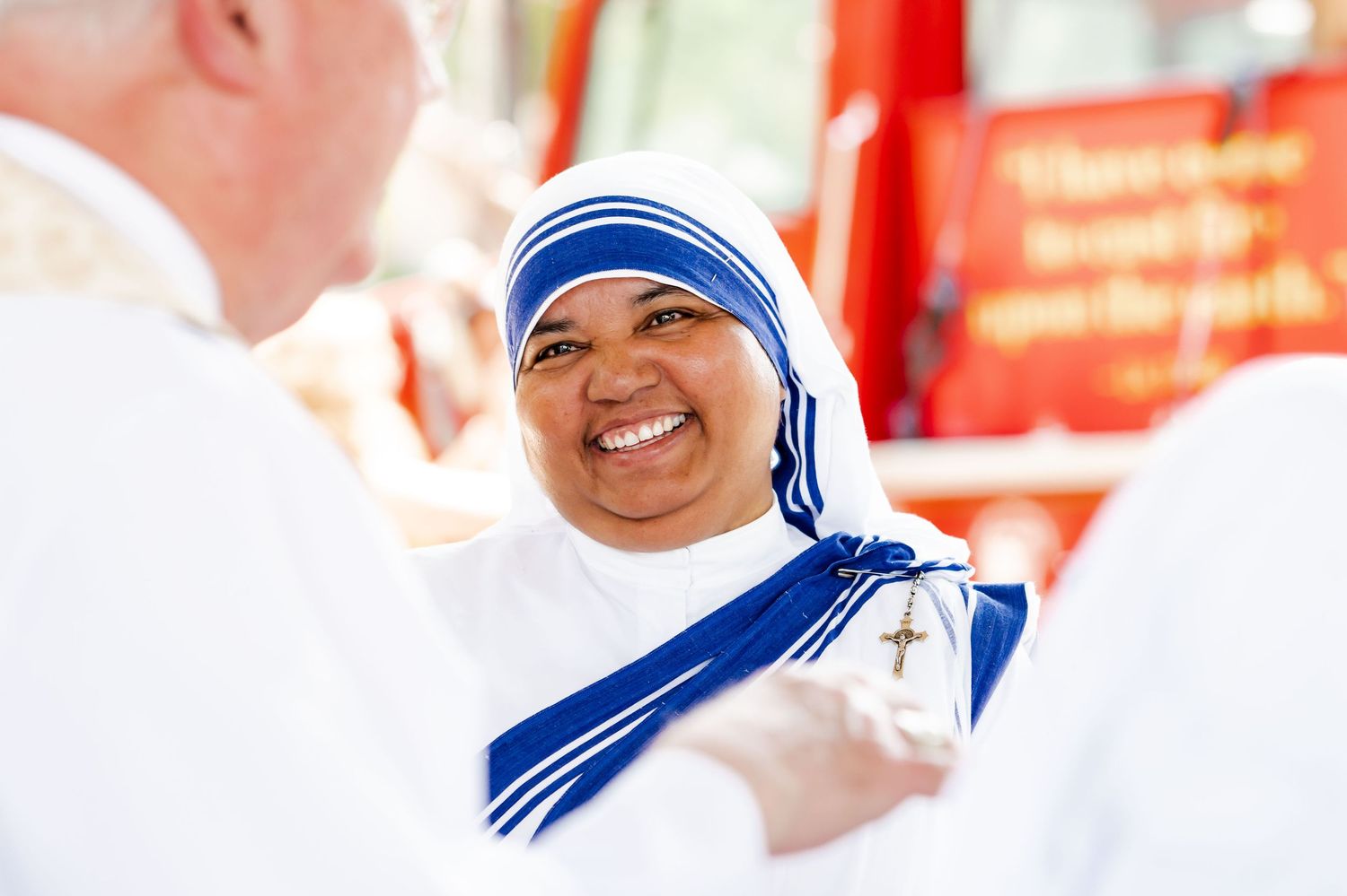 A religious sister wearing a distinctive blue and white habit smiles warmly during a ceremony.