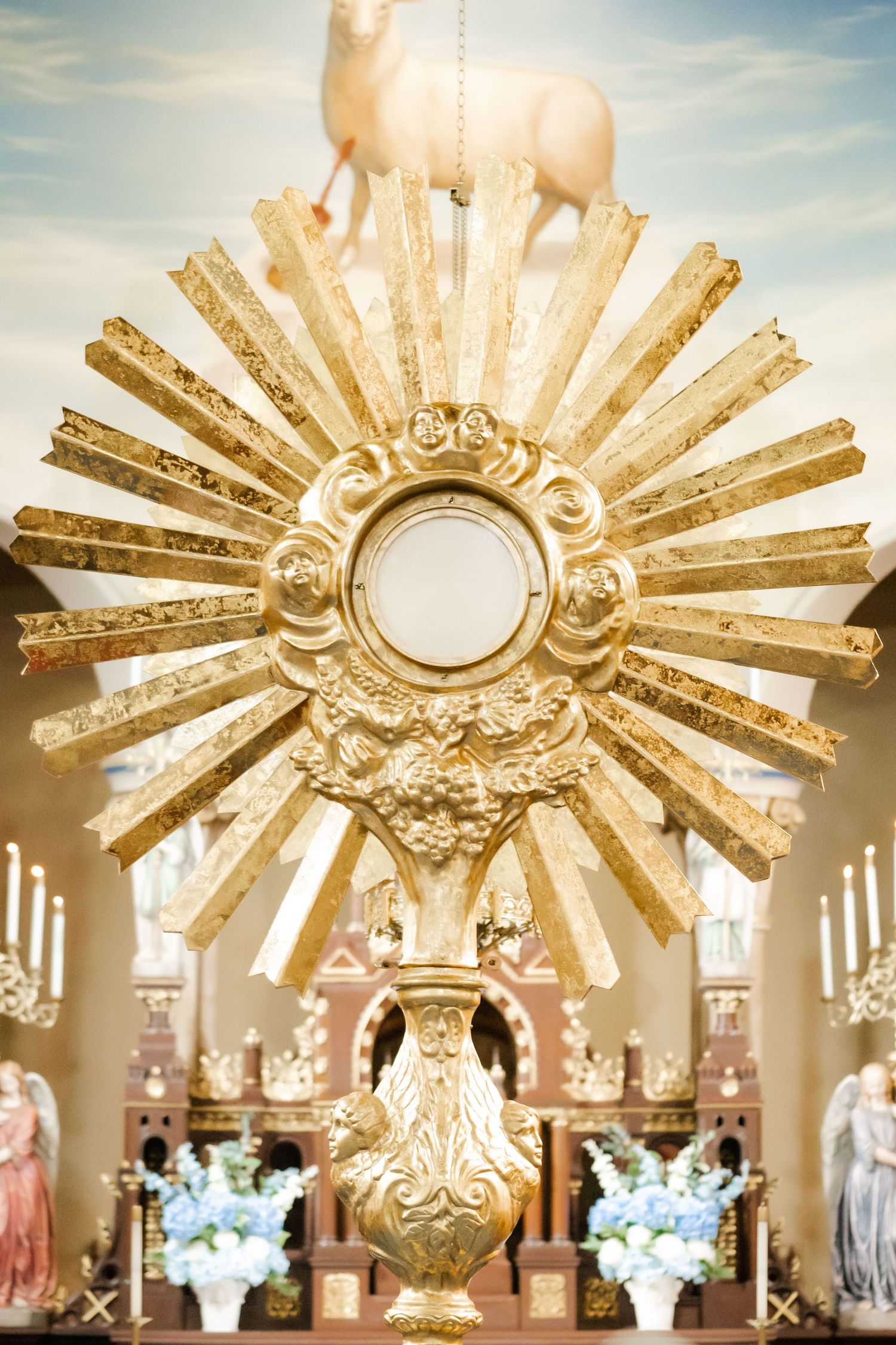 Golden ornate monstrance with sunburst design displayed in a church setting with floral decorations.