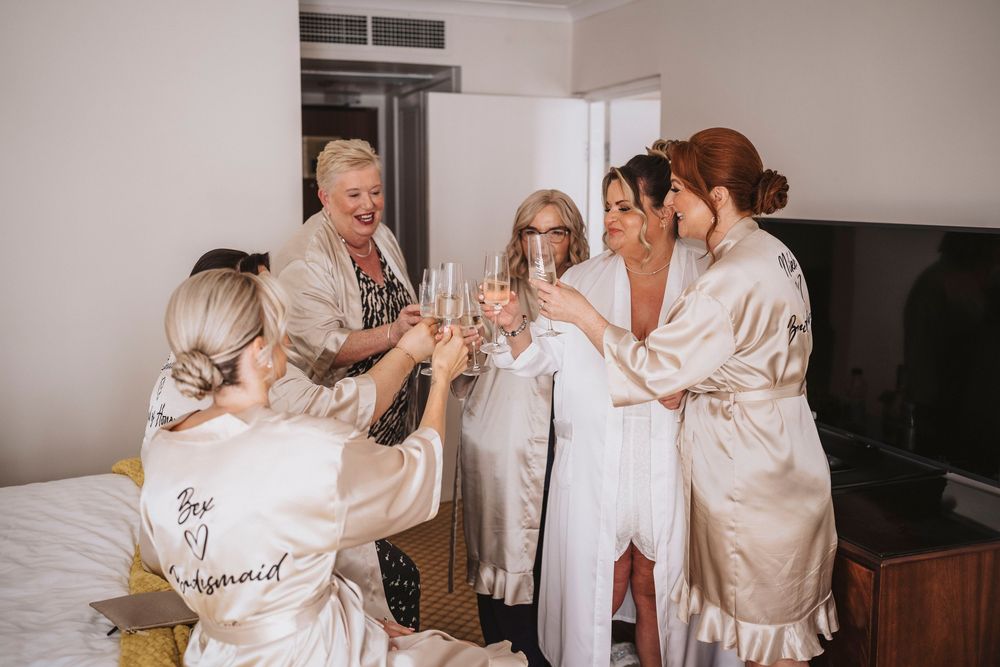 A group in matching silk robes toasts with champagne glasses during a pre-wedding celebration.