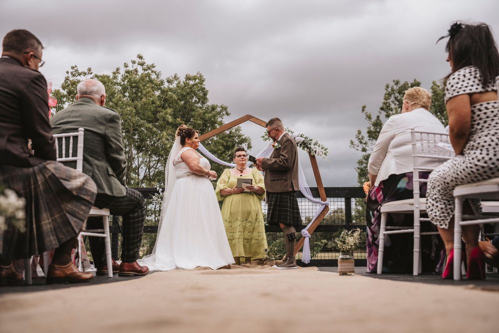 Low-angle view of an outdoor wedding ceremony with guests seated in white chairs under cloudy skies.