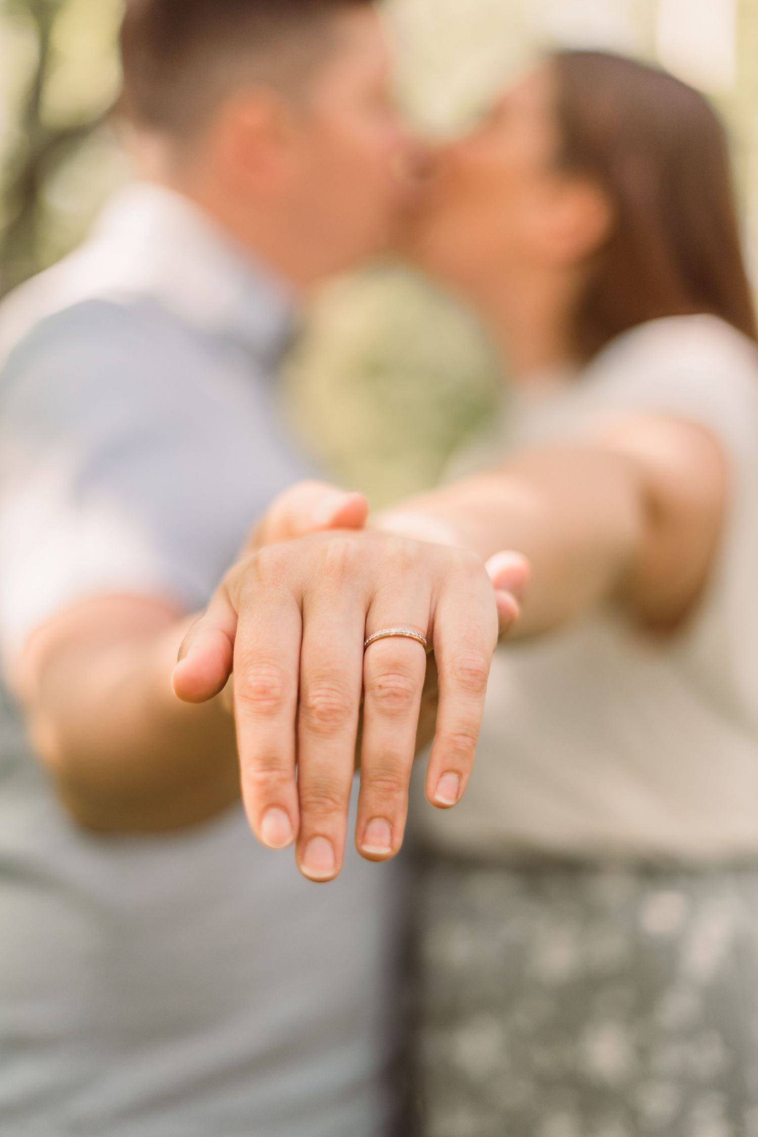 A close-up shot of an engagement ring on an outstretched hand with a blurred romantic background.