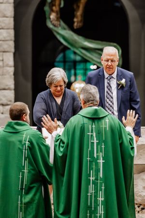 Two clergy members in green robes with cross designs are performing a religious ceremony inside a stone church.
