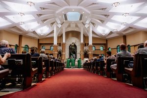 A wedding ceremony takes place in an elegant chapel with ornate ceiling details and a red carpeted aisle.