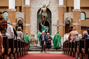 A church wedding ceremony takes place in a grand cathedral with ornate columns and a large crucifix statue at the altar.