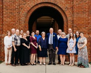 A group gathers for a formal photo under a red brick archway entrance of a building.