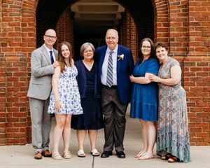 A group of six people standing together under a brick archway wearing formal attire at a special occasion.