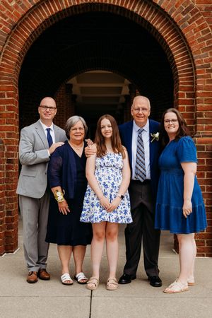 A family group poses together under a brick archway entrance wearing coordinated formal attire in blue and neutral tones.