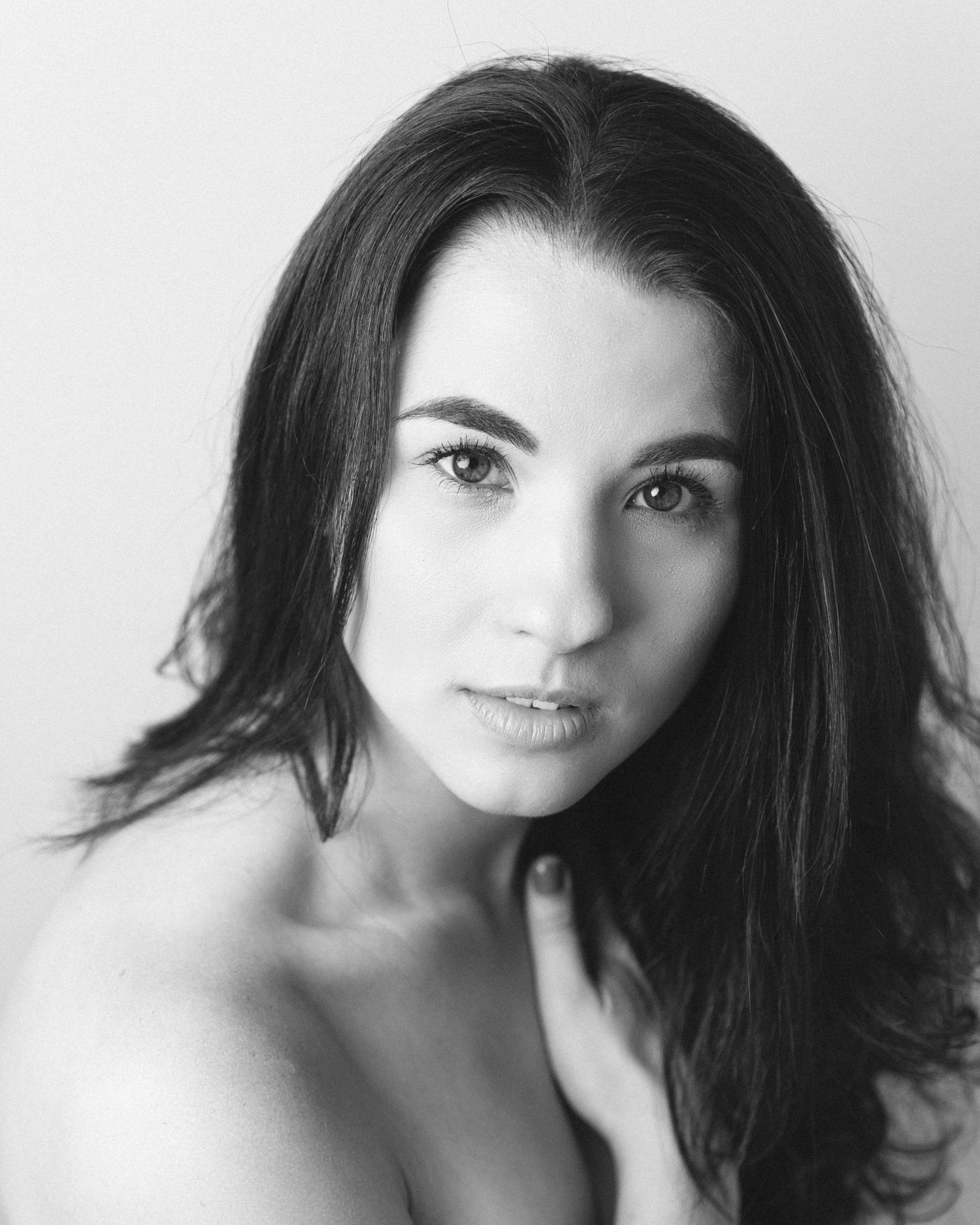 Dramatic black and white portrait featuring dark hair and bare shoulders against neutral background.