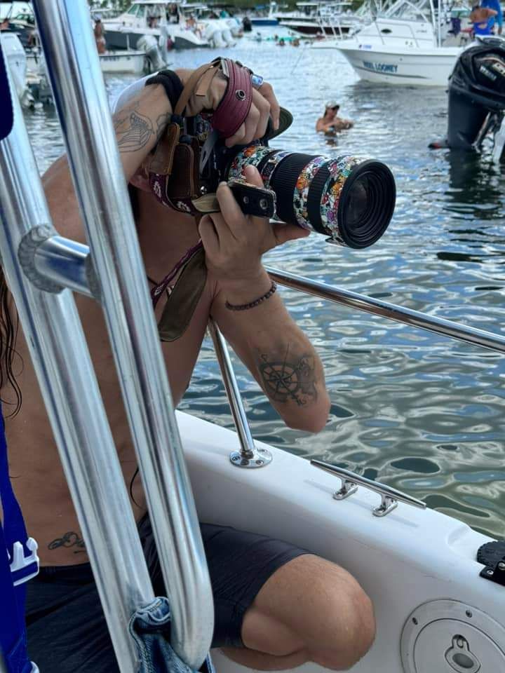 Person with tattoos relaxing on a boat in the water surrounded by other vessels on a sunny day.