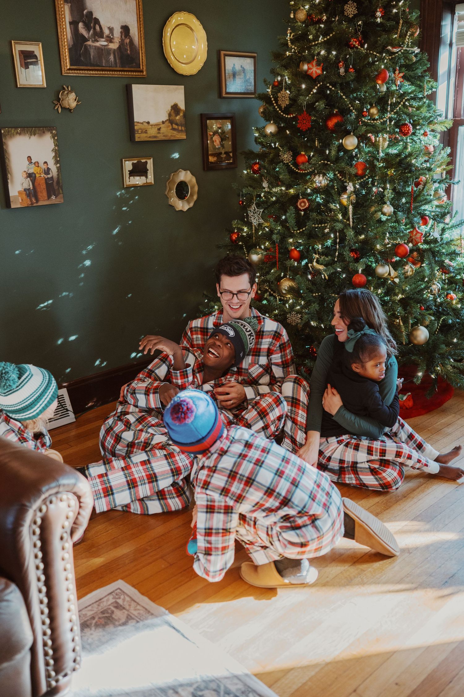 A family wearing matching plaid pajamas sits together by a decorated Christmas tree in a cozy living room.