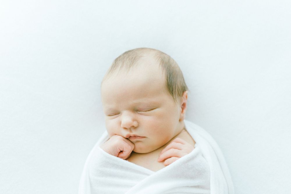 Sleeping baby swaddled in white with serene expression on light background.