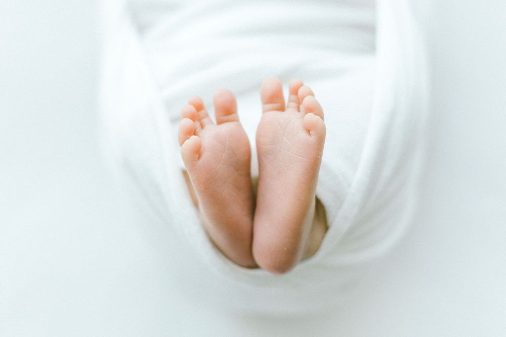 Tiny baby feet peeking out from white swaddle wrap against bright background.