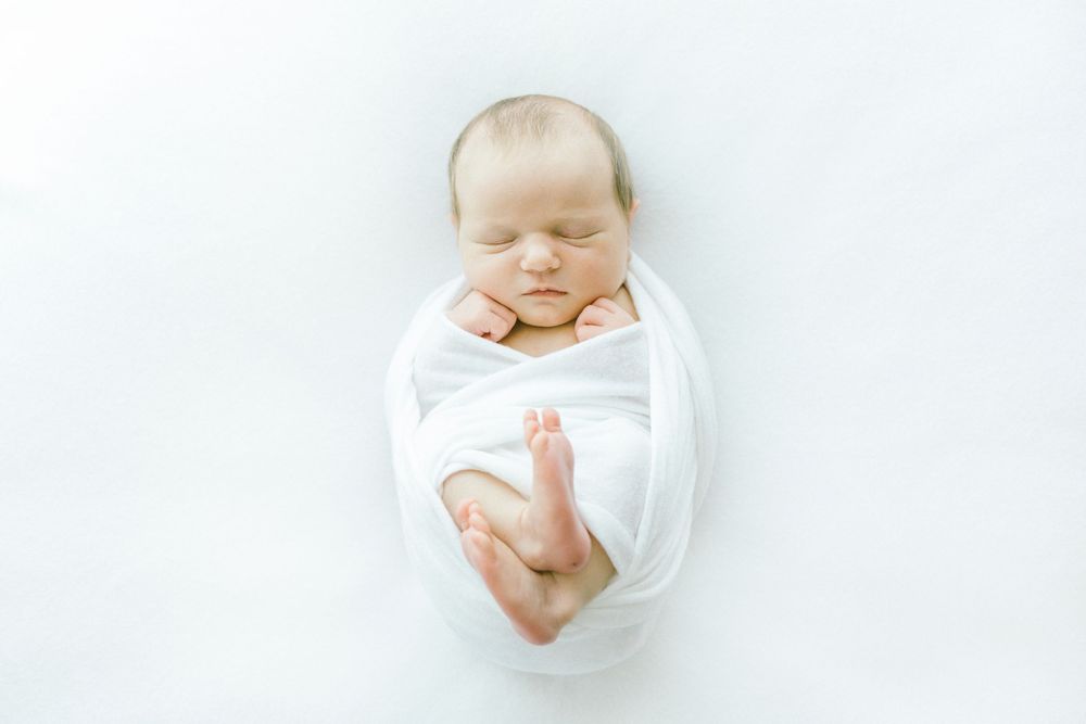 Peaceful newborn resting in white swaddle against minimalist light setting.