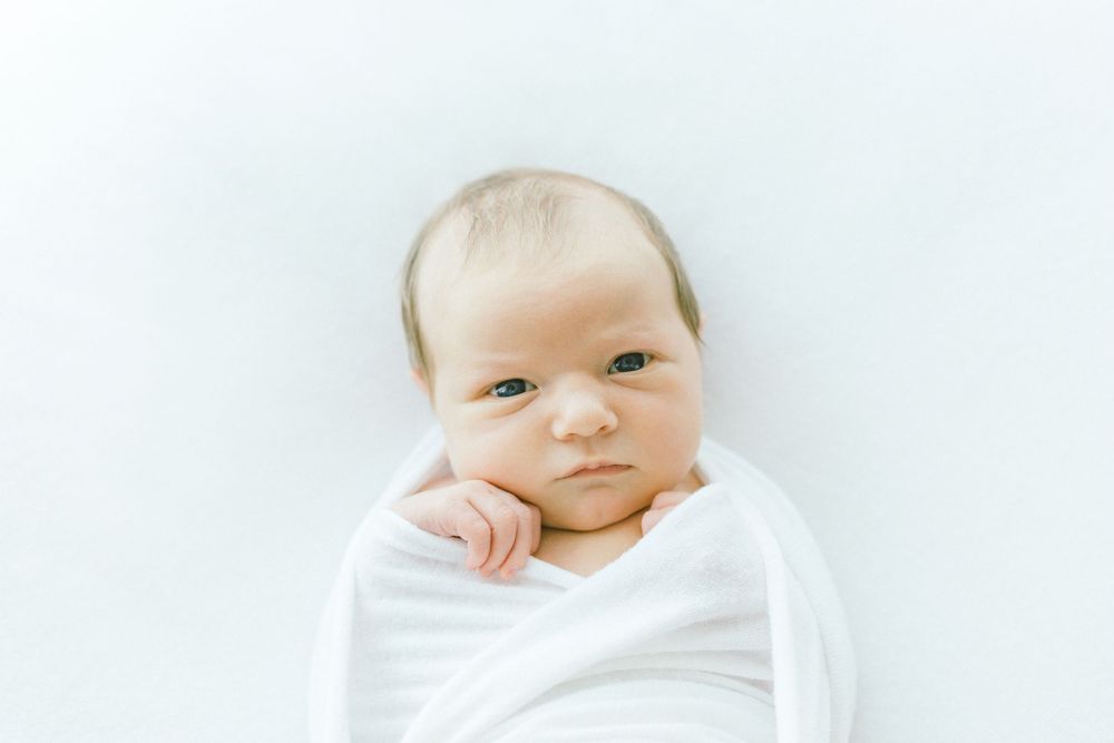 Newborn baby peacefully sleeping wrapped in soft white fabric against light background.