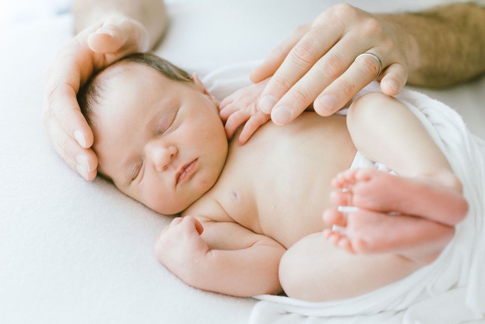 Gentle interaction with sleeping newborn wrapped in soft white fabric.