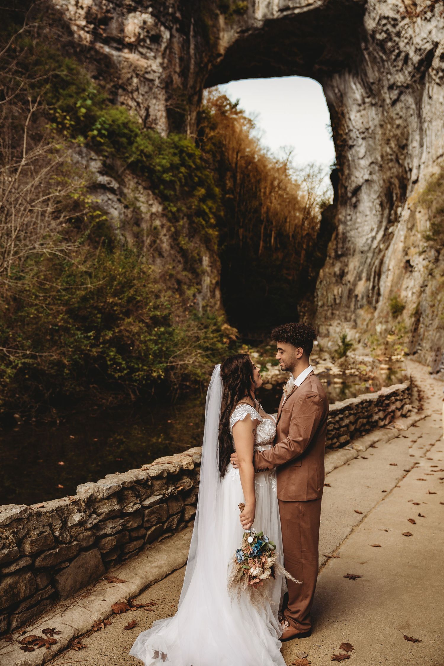 A romantic first look moment unfolds against a stone wall backdrop in natural lighting.