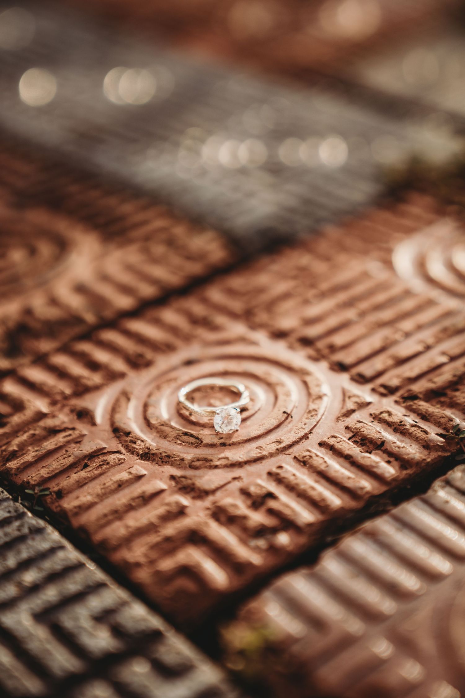 Close-up of diamond engagement ring on textured copper surface.