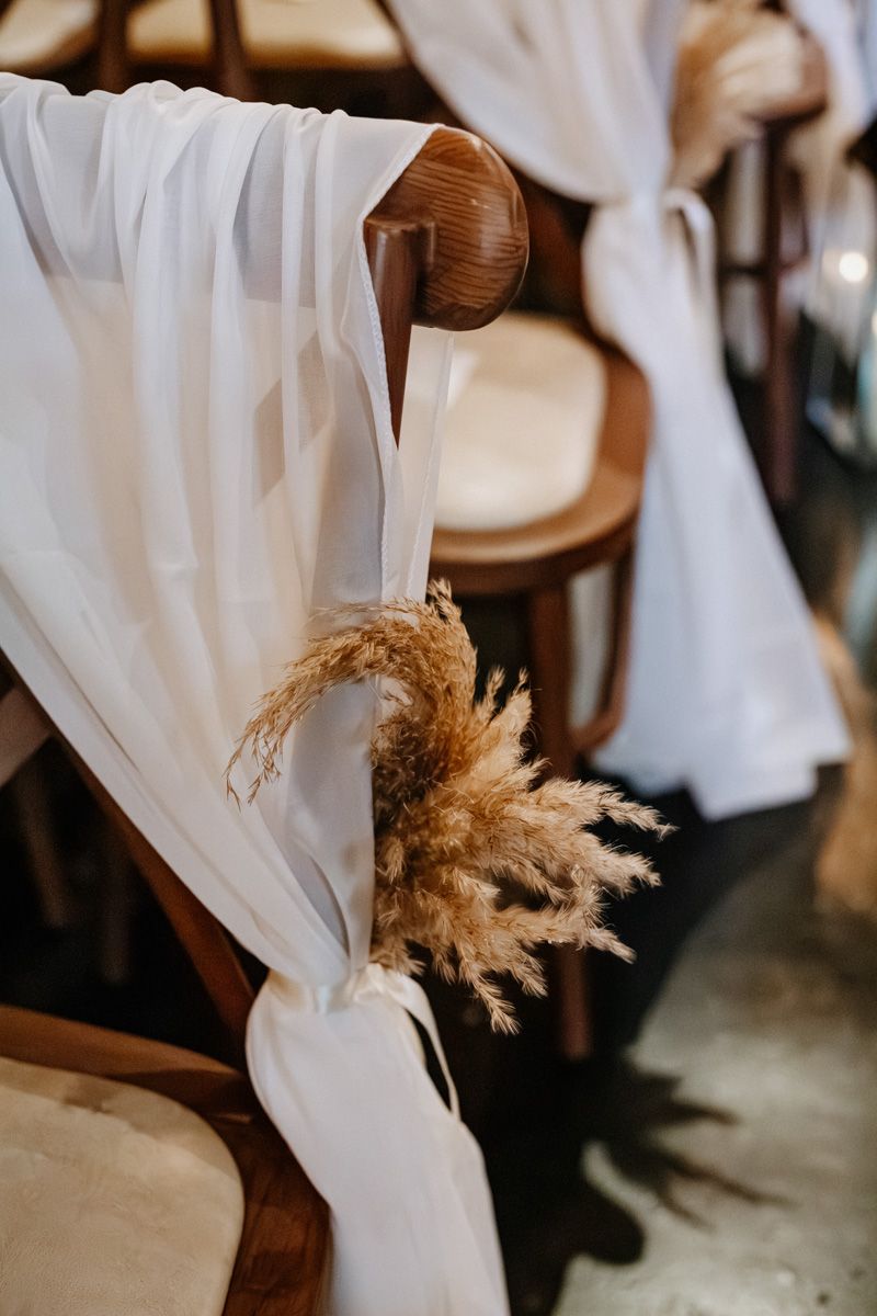 White fabric chair sashes with dried pampas grass accents create an elegant wedding ceremony setting.