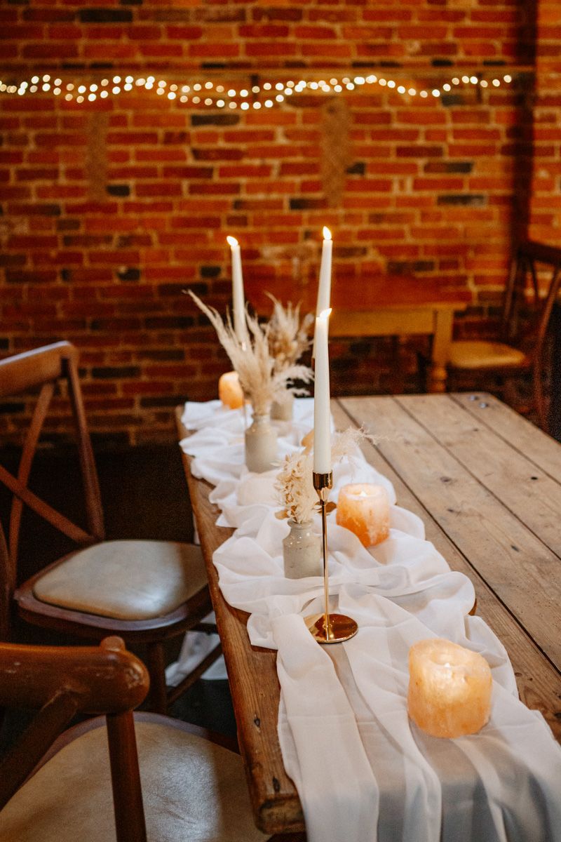 White table setting with glowing candles and string lights against exposed brick wall creating romantic ambiance.