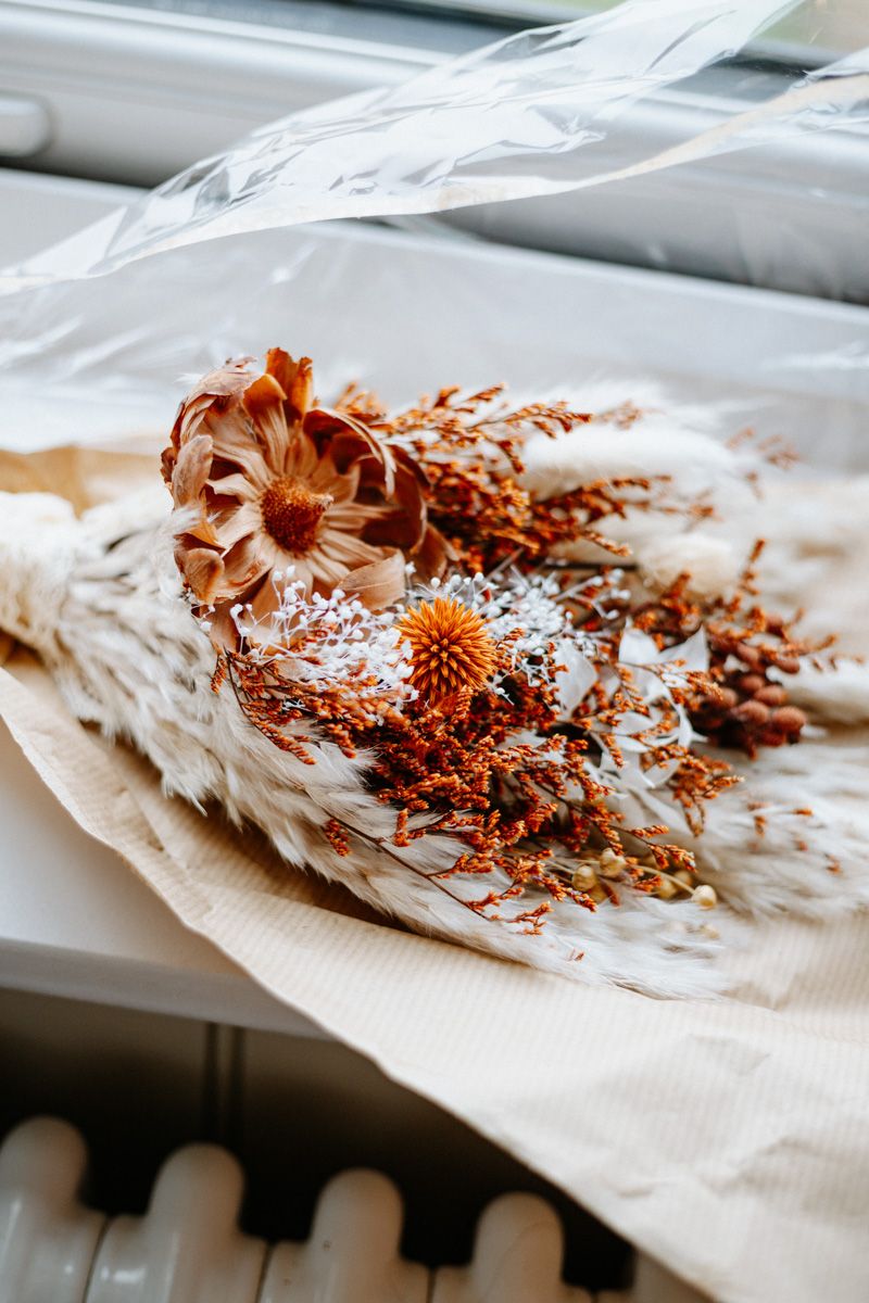 Dried floral arrangement with copper and neutral tones laid on white fabric.