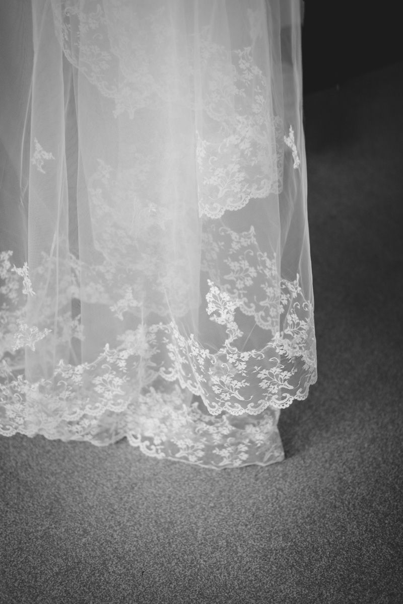 Delicate lace trim detail of white wedding dress fabric against dark background.