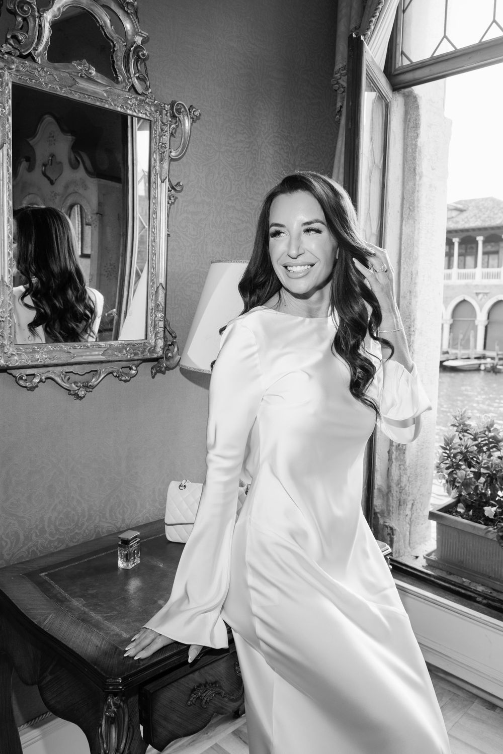 A series of black and white photos showing someone in a white dress posing by a window with ornate mirrors. Book your Venice photoshoot