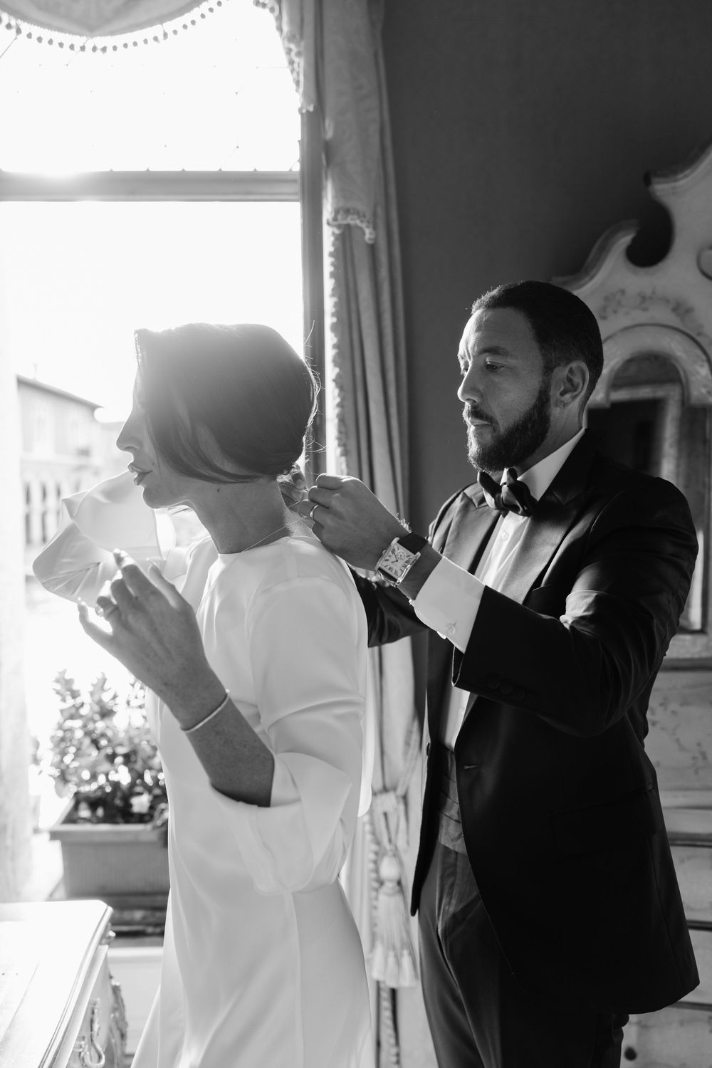 Two people in contrasting black and white attire stand together in a room with natural light streaming through windows. Venice photographer