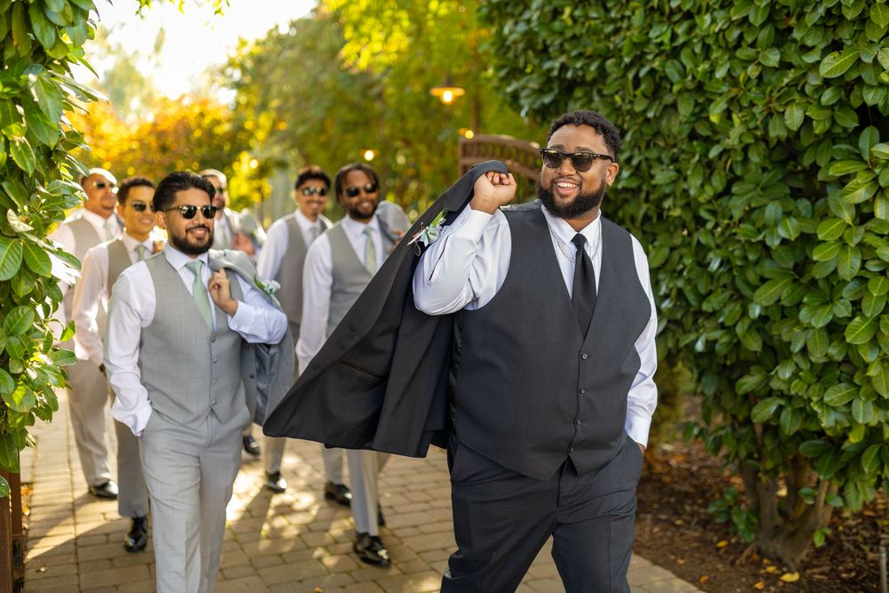 Wedding party members in formal attire walking through a lush garden pathway.