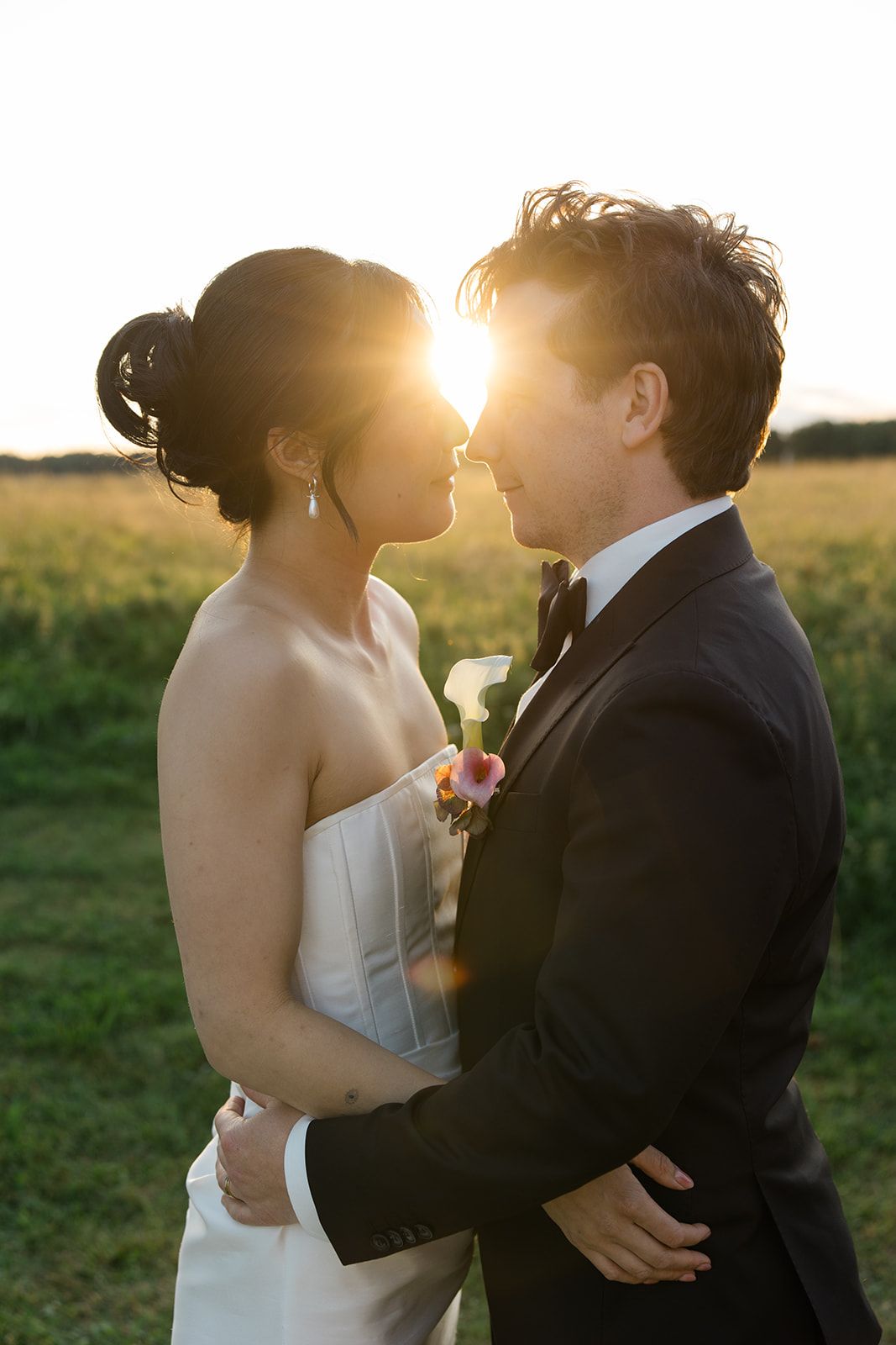 A romantic wedding couple shares intimate kisses in a golden sunlit field at sunset.