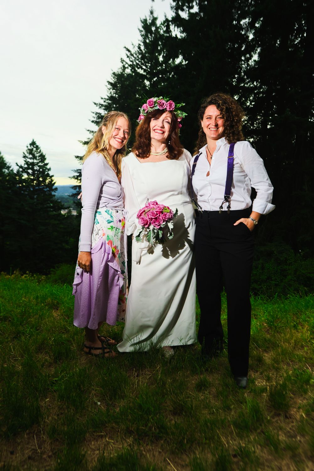 Three people in casual attire pose together in an outdoor setting with trees and grass in the background.